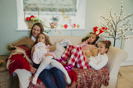 Three little girls are relaxing on the sofa with their mother at christmas time, watching the television.の写真素材
