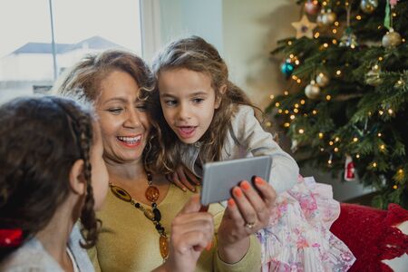 Grandmother is taking selfies on a smartphone with her granddaughters at christmas time.の写真素材