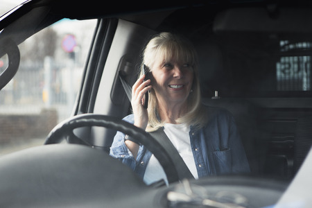Senior woman is having a conversation on the phone before going somewhere in her car.の写真素材