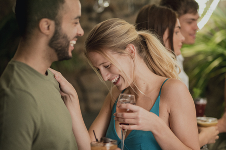 Couple enjoying cocktails in a bar at a social event. They are laughing and embracing.の写真素材