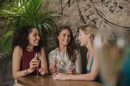 Three women are enjoying socialising over drinks in a bar. の写真素材