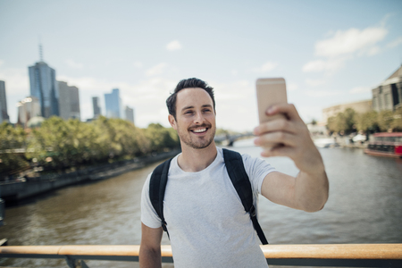 Millennial tourist is taking a selfie from a bridge in Melbourne, Victoria with the cityscape in the background. の写真素材