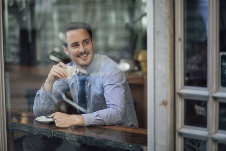 Millennial businessman is laughing while enjoying a cup of coffee in a cafe before work.の写真素材