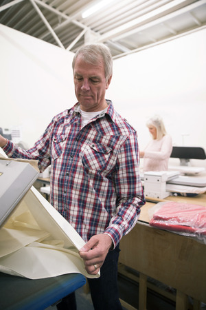 Senior man is pressing fabric in a business warehouse. の写真素材