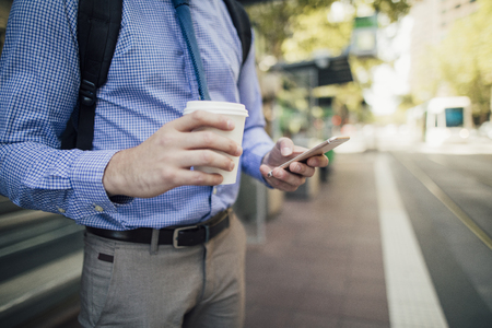Close up shot of a businessman holding a coffee cup and a smart phone while commuting in Melbourne, Victoria.の写真素材