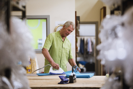 Senior man is ironing fabrics in the business factory. の写真素材