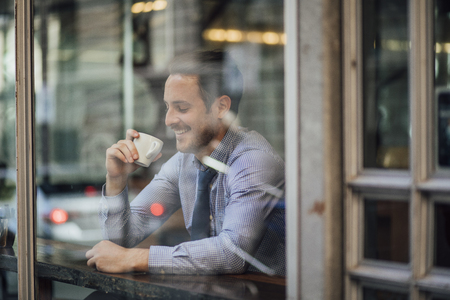 Millennial businessman is laughing while enjoying a cup of coffee in a cafe before work.の写真素材