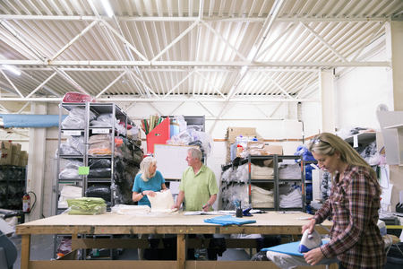 Businesspeople are working together in a textile warehouse. Onbe person is ironing fabric while the others are stocking fabric and material.の写真素材