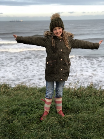 Little girl is posing in front of the sea at the beach. she has her arms outstretched and is looking at the camera.の写真素材