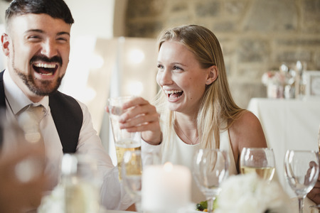 Wedding guests are enjoying themselves while sitting at the table for the meal. They are talking and laughing while drinking wine and lager.の写真素材