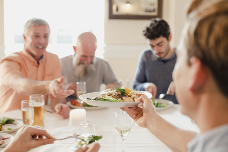 A table of male guests are eating at a wedding dinner together, One of the men is passing his plate to someone else to try. の写真素材