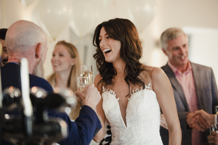 Beautiful bride is socialising with her father and family on her wedding day. They are drinking champagne and laughing together.の写真素材