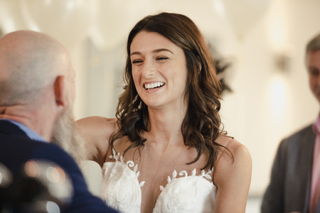 Beautiful bride is sharing a dance with her proud father. They are laughing with their arms around each other. の写真素材