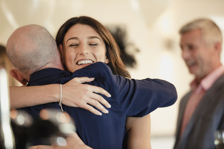 Beautiful bride is sharing a dance with her proud father. They are laughing while hugging with their arms around each other.の写真素材