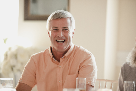 Happy senior man at a wedding. He is sitting at a table, laughing with guests out of the frame.の写真素材