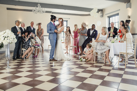 Beautiful couple are sharing their first dance on their wedding day. All of their guests are sitting around the dancefloor watching them. の写真素材