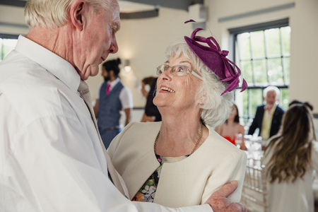 Senior couple are sharing a dance at a wedding. They are looking lovingly at each other while they dance. の写真素材