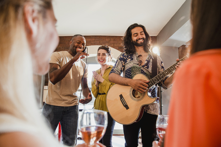 Two young men and a young woman are singing and playing guitar at an entertainment venue to a crowd. の写真素材