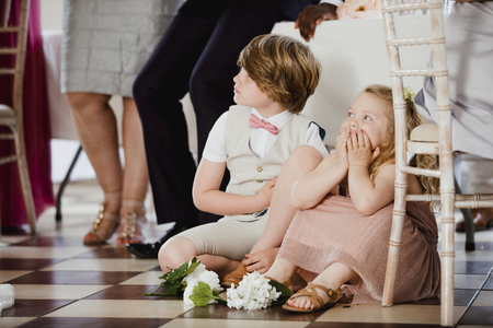 Children are sitting on the dancefloor by a table at a wedding. They are watching the bride and groom share their first dance. の写真素材