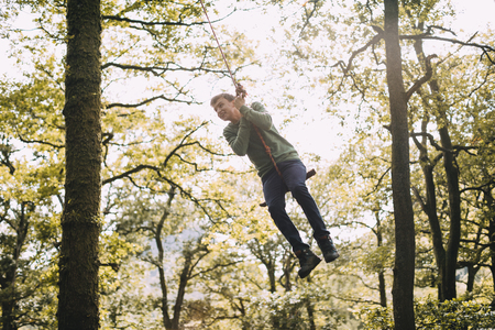 Teenage boy is having a turn on a rope swing which he has found in the woodlands while hiking. の写真素材