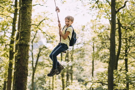 Little boy is having a go on a rope swing he has found while hiking. の写真素材