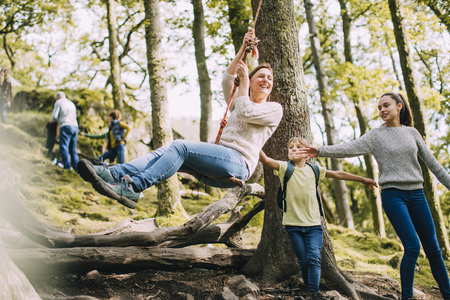 Mature woman is being pushed on a rope swing by her children while they are out on a hike. の写真素材