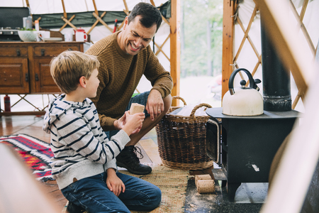 Little boy and his father are placing firewood in the chiminea of the yurt they are staying in on a holiday.の写真素材