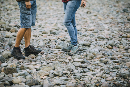 Legs of a mature couple on a pebble beach. They are holding skimming stones. の写真素材