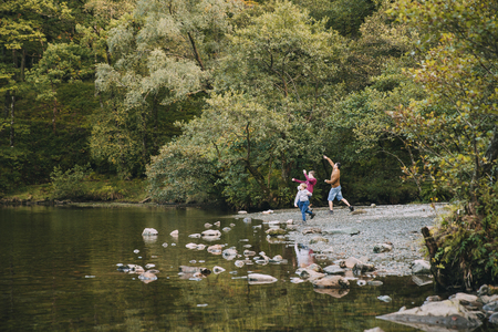 Two boys are skimming stones in a lake with their father. の写真素材