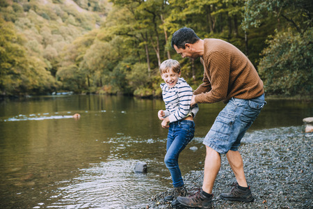 Little boy and his father have been hiking and found a pond. His father is holding the boy, teasing to throw him in the water. の写真素材