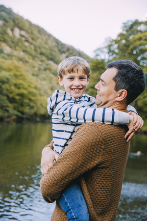 Little boy is smiling for the camera while being held by his father. They are standing near a lake.の写真素材