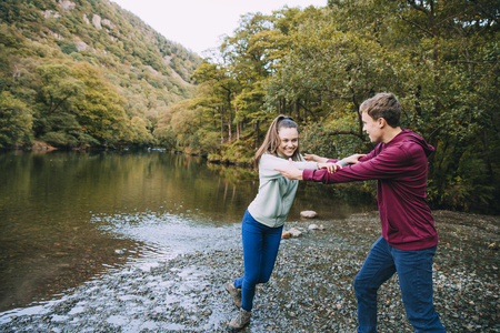 Teenage boy is being pushed away by his sister as he is trying to push her in to a lake they have found while hiking. の写真素材