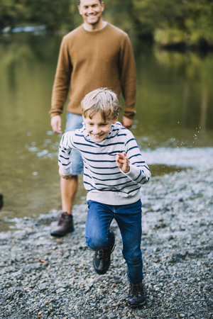 Little boy is being chased near the lake by his father while they are out hiking. の写真素材