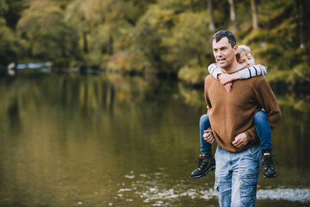Little boy is receiving a piggyback from his father while they are hiking through the Lake District.の写真素材