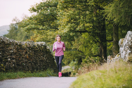 Senior woman is running along a trac path in the Lake District with a water bottle.の写真素材
