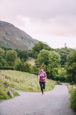 Senior woman is running along a trac path in the Lake District with a water bottle.の写真素材