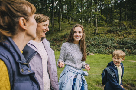 Teenage girl and her little borther are talking to their mother and grandmother as they hike through the woodlands together.の写真素材