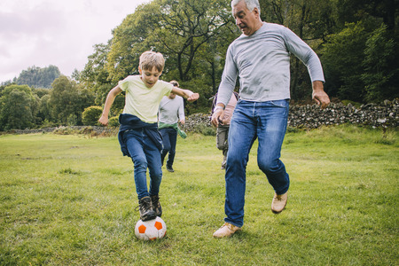 Three generation family are playing football together in a field. There are two boys, their father and their grandfather.の写真素材