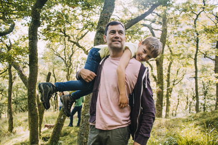 Little boy is smiling at the camera as he is being fireman carried by his father through the woodlands. の写真素材