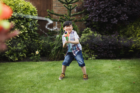 Little boy is having a water fight in the garden with his family. He is making a face as he gets hit with a water pistol in his hand.の写真素材