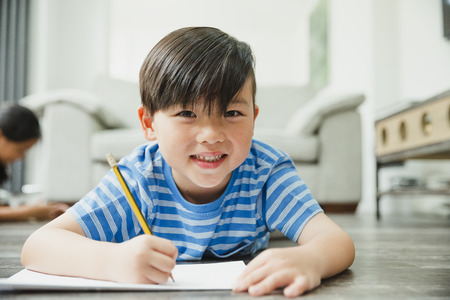 Little boy is smiling for the camera while lying on the floor as he is doing his homework. の写真素材