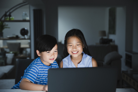 Little girl and her younger brother are using the laptop together in their home at night. の写真素材