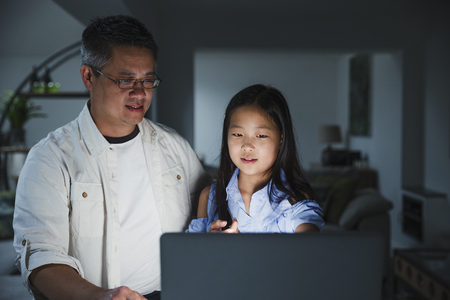 Little girl is getting help from her father while doing homework on the laptop at home. の写真素材