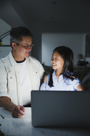 Little girl is getting help from her father while doing homework on the laptop at home. の写真素材
