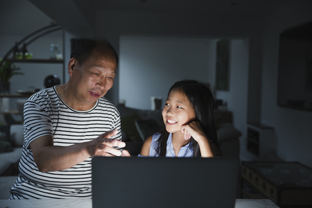 Little girl is laughing as her grandfather tries to understand how to use her laptop. の写真素材