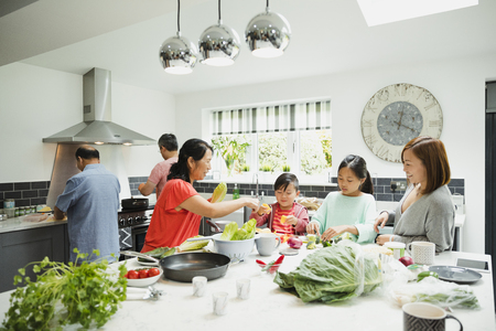 Three generation family are preparing vegetables for a stir fry in the kitchen of their home together. の写真素材