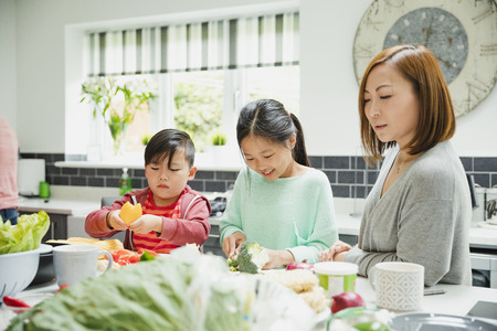 Mother is guiding her children as they help prepare vegatables for their stir fry dinner. The little girl is cutting broccoli and the boy is cutting peppers. の写真素材