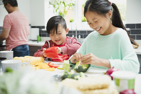 Little girl and her brother are helping their family to prepare a stir fry dinner. They are cutting up pepper and broccoli. の写真素材