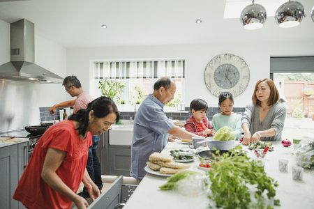 Three generation family are preparing vegetables for a stir fry in the kitchen of their home together. の写真素材
