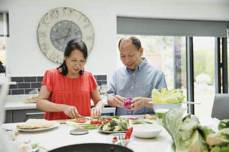 Senior couple are preparing vegetables together in the kitchen to make a stir fry.の写真素材